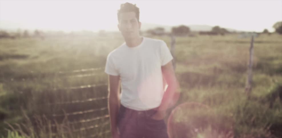 Man stands in front of a fence and a grassy field on a sunny day