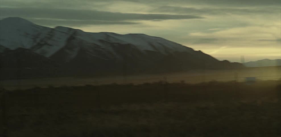 A snow capped mountain is next to a field as the sun shines