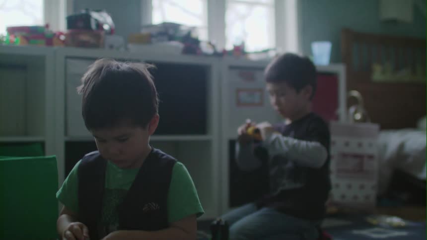 Two boys play with toys on the floor of a bedroom