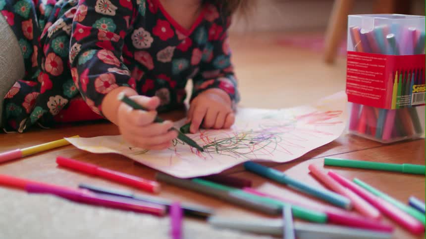 A young girl draws on paper with markers