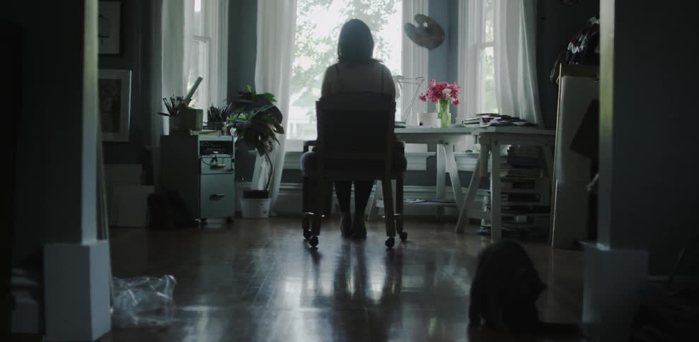 A woman is sitting quietly in a chair as a cat cleans itself
