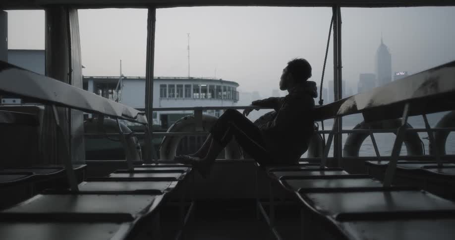 A man is sitting on a ferry crossing a harbor