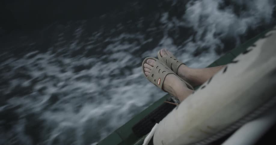 A person hangs their feet over the edge of a moving boat