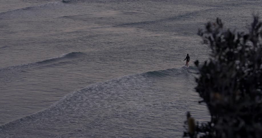 Waves flow out with the tide as a man rides a surfboard