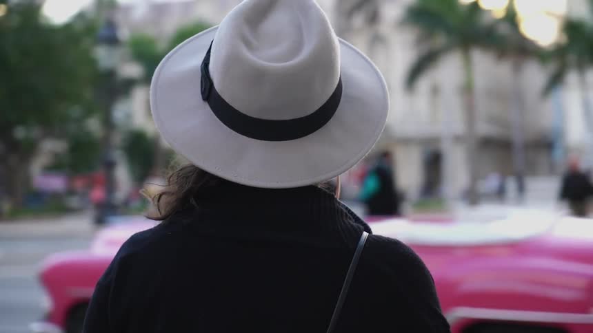 A woman walks on a city sidewalk with pedestrians and cars all around