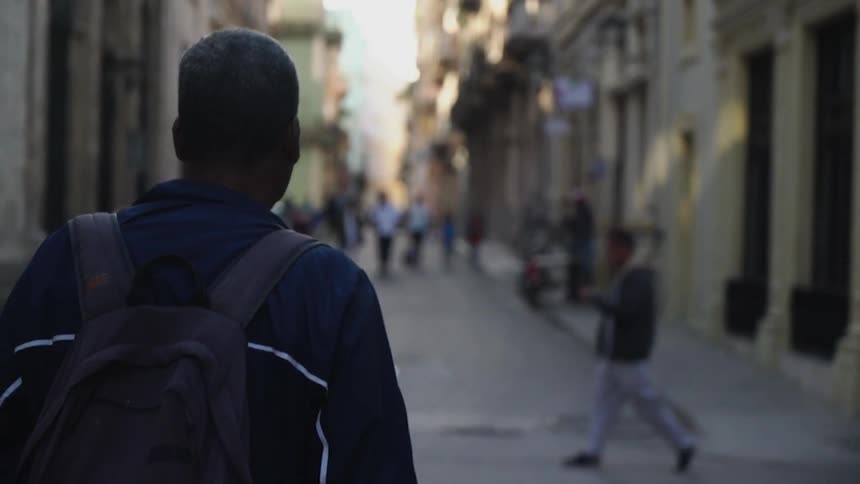 Man wearing a backpack walks down an alleyway towards a group of people