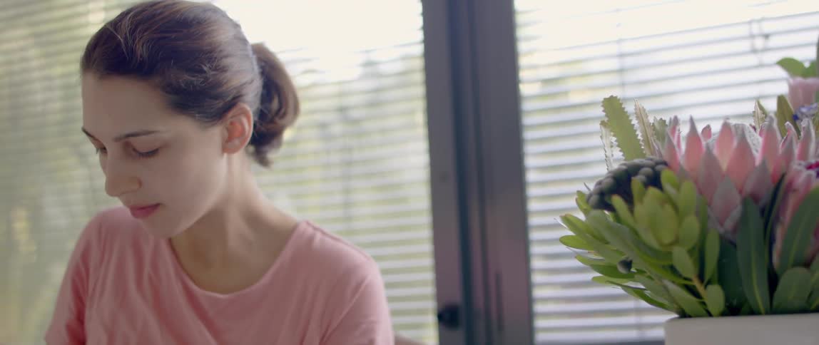 A woman sits in front of a window indoors