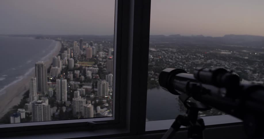 A telescope is pointing out of a high-rise window toward a beach