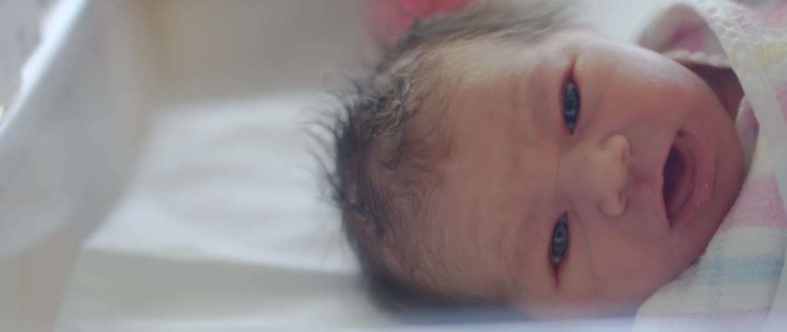A newborn lays swaddled in a bassinet