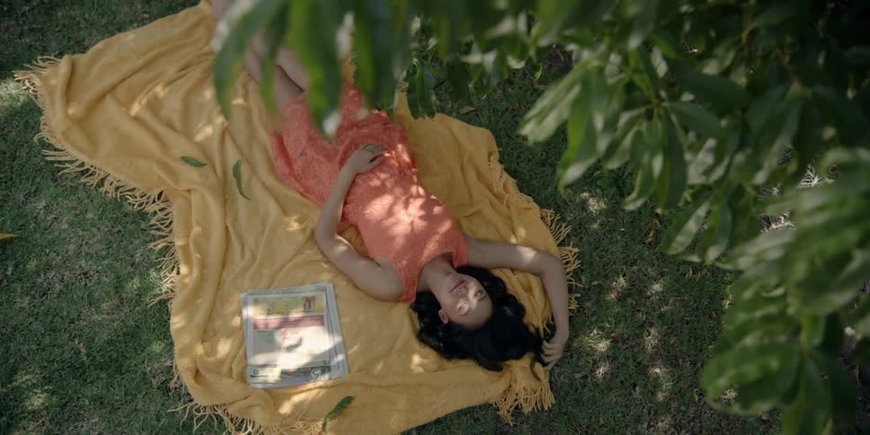 Woman lays on a yellow blanket outside under a tree