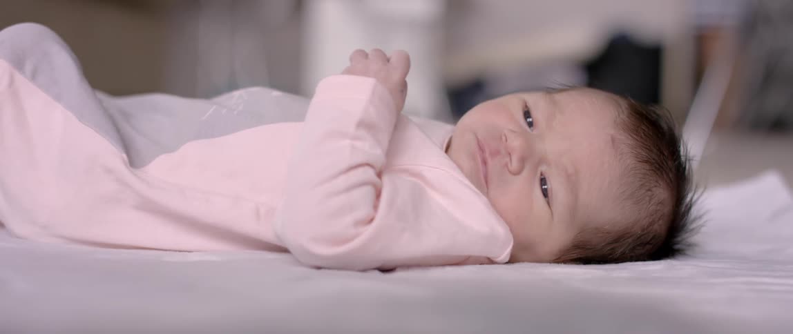 A baby is moving its arm and looking about as it is lying down