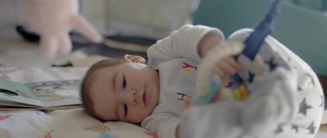 Baby lays on a blanket waving hands in front of a swinging toy