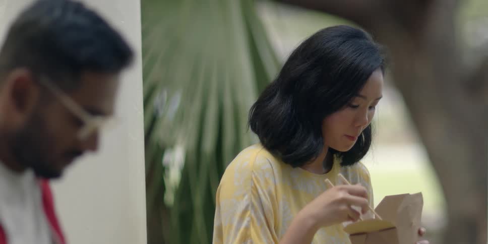 A woman eating noodles smiles at a man who sits next to her