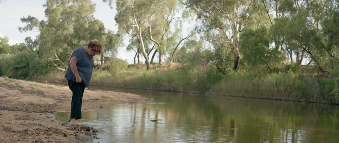 A woman walks barefoot into a river
