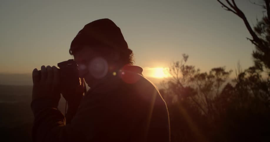 A man is taking photographs on a hill at dawn