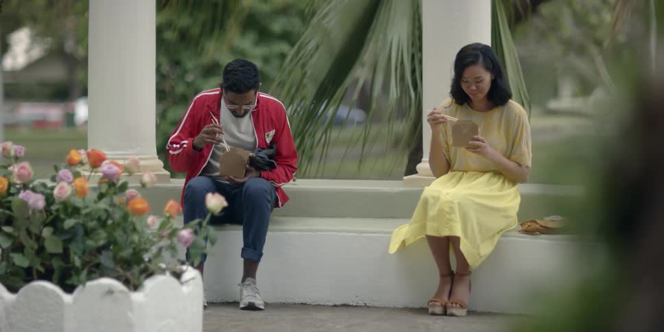 Man and woman eat chinese food on a ledge outside of a building