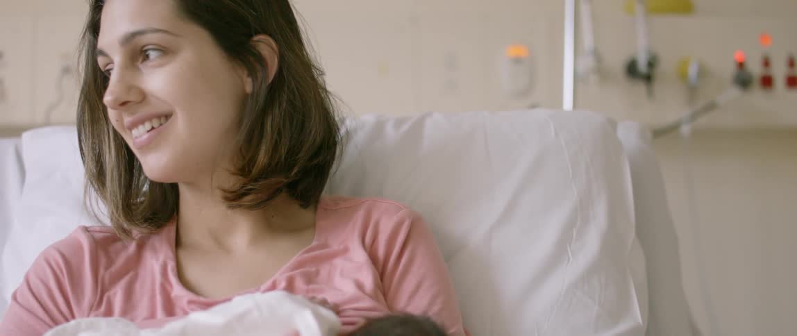 A woman sitting in bed with her baby smiles