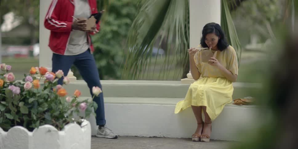 A man and woman sit outside and eat takeout with chopsticks