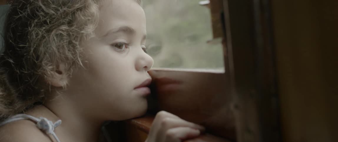 A little girl is watching out of a window on a moving train