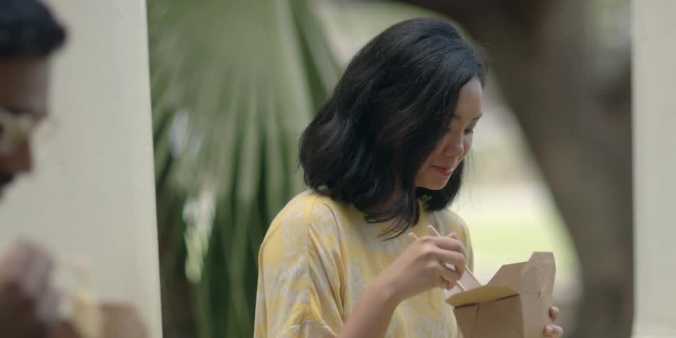 A woman eating from a tray looks over at a man