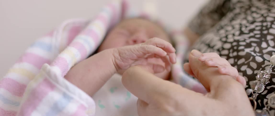 Crying infant holds an adult's fingers