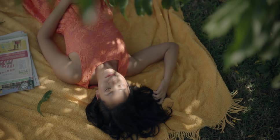 A woman plays with her hair as she lies resting on a picnic blanket