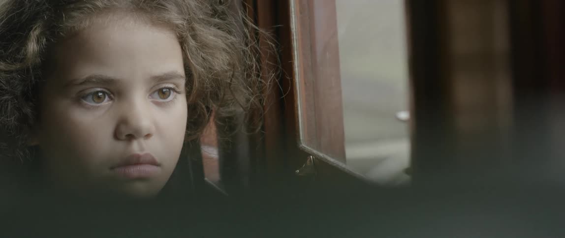 A little girl is staring vacantly out a window