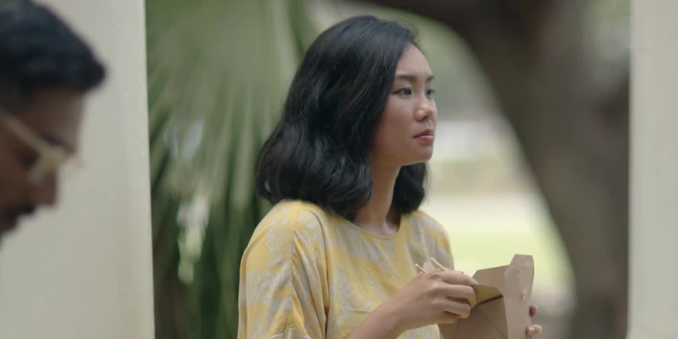 A man and woman sit outside and eat takeout with chopsticks