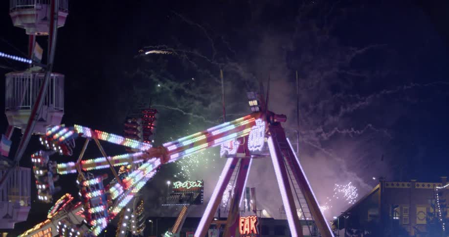 Fireworks explode behind amusement park rides at night