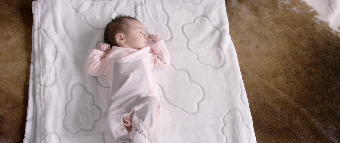 A baby lies on a blanket on the carpeting