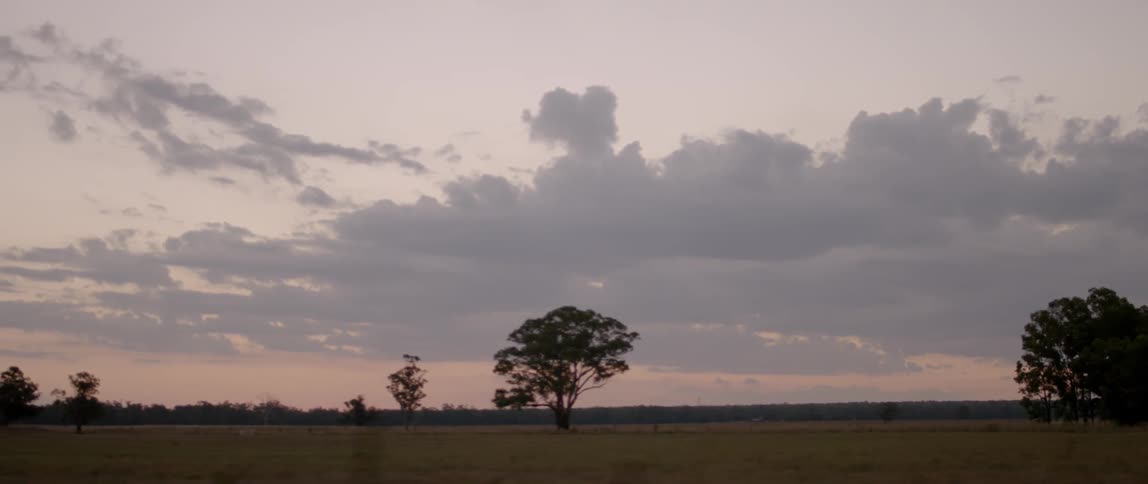 A vehicle drives on a rural road at sunset