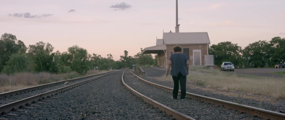 Woman walking down railroad tracks towards a depot