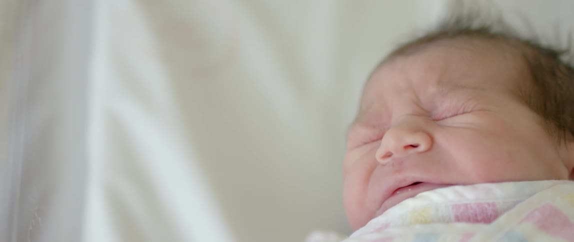 A swaddled newborn opens its mouth and yawns
