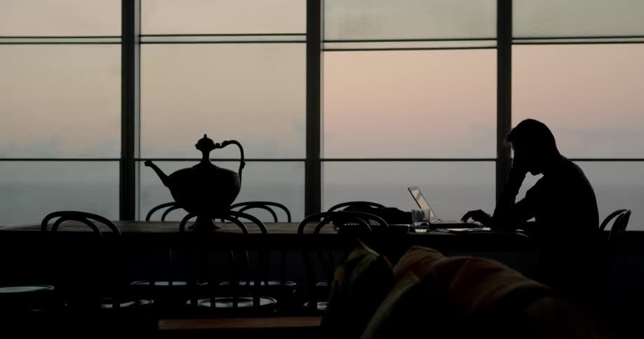 A man is using his laptop near the large window