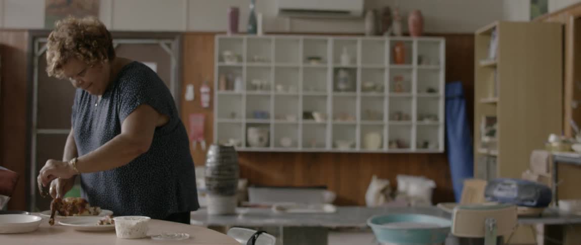 A woman stands at a table and cuts up a cooked chicken