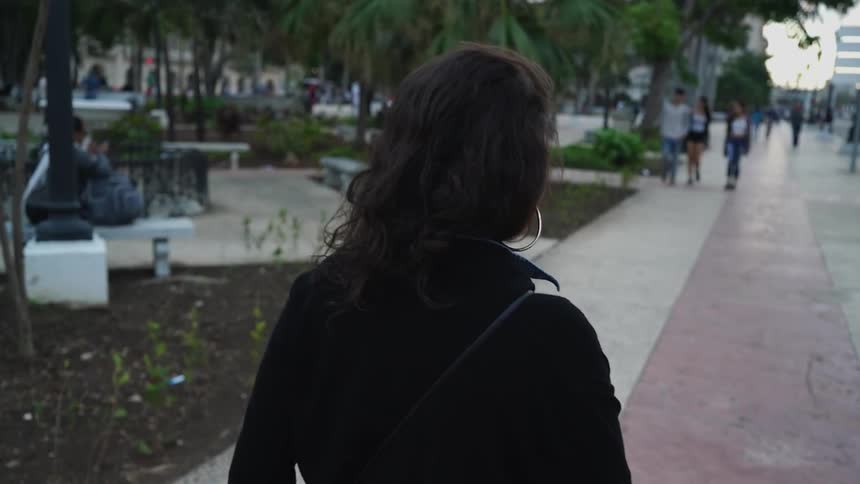 A woman with dark hair and hoop earrings walks down a sidewalk