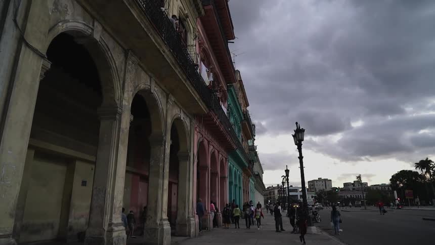 Pedestrians stand on a city sidewalk on a cloudy day
