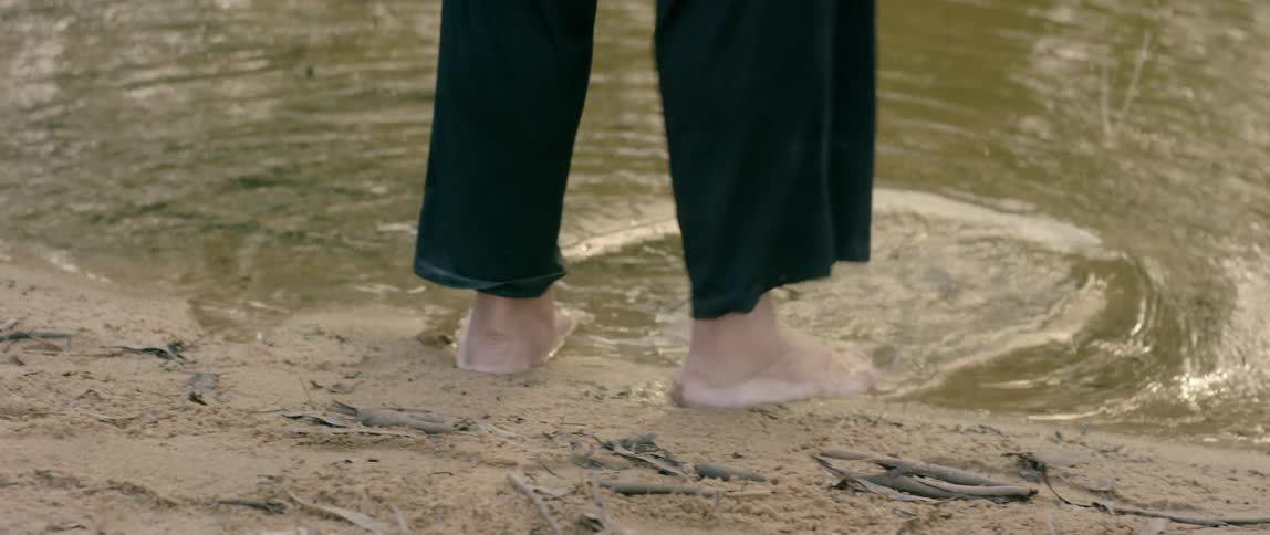 A person hikes up their pants and walks into pond water