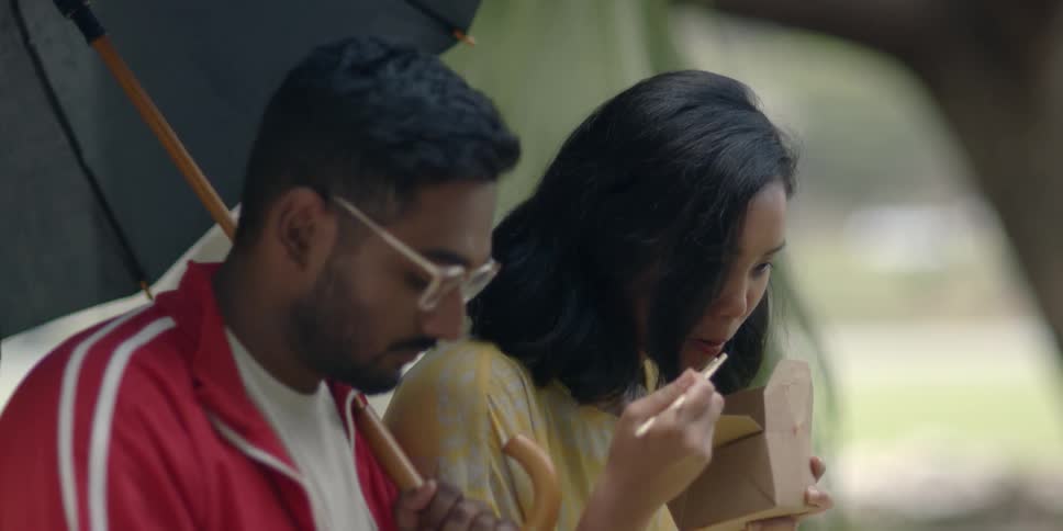 A man and woman eat noodles under the umbrella
