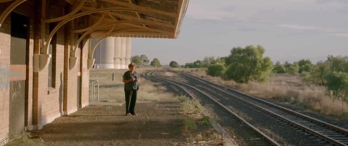 A woman stands at a train station on a sunny day