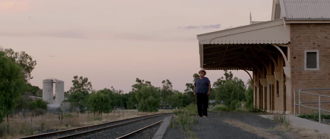 Woman stands next to railroad tracks outside a train depot