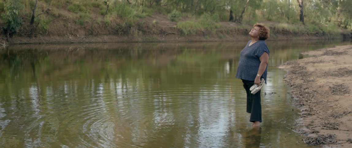 A woman stands barefoot in a river as water ripples around her