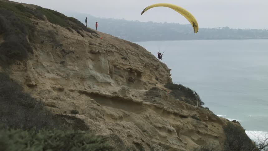 Someone paragliding off an ocean-side cliff as two people watch