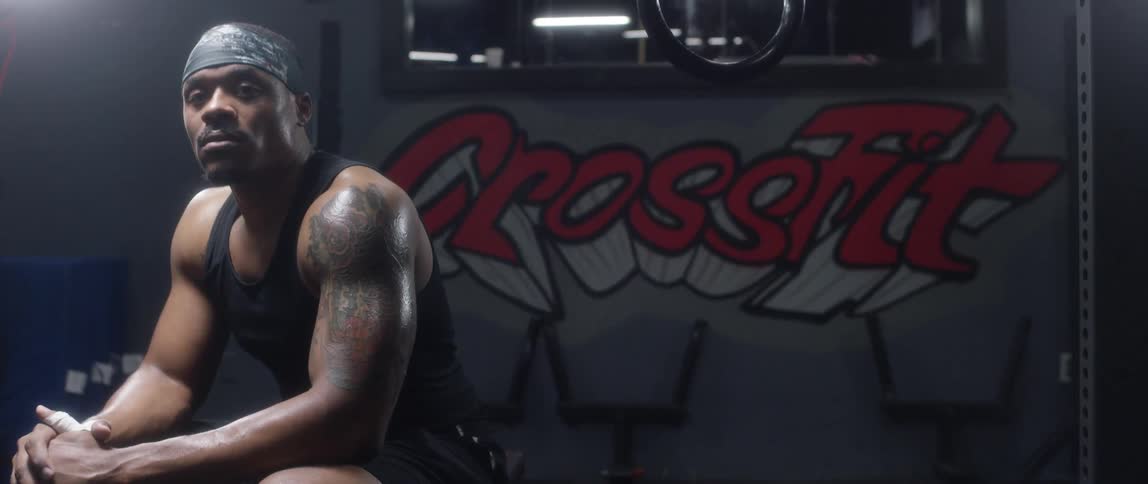Muscular tattooed black man with a bandana sits on a bench and looks at the camera