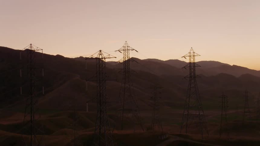 Flying over dense power lines in a mountain valley at sunset