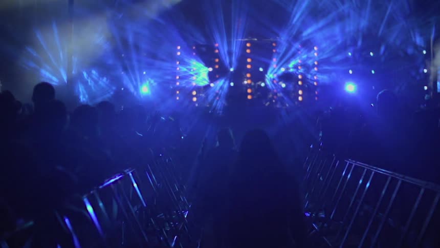 Walkway with large crowd on either side and strobe lights up ahead