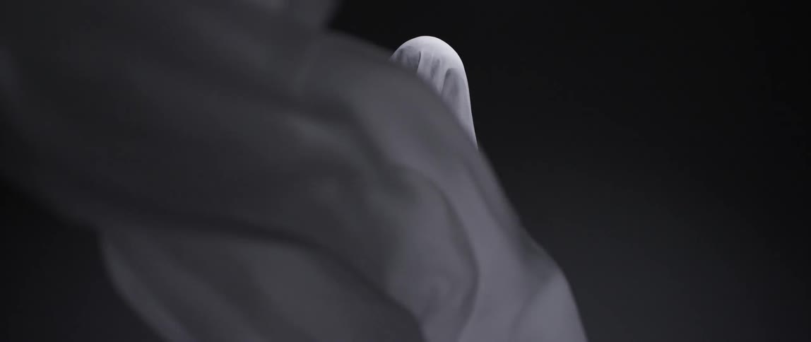 A sheet blowing in the wind then falls to reveal a shape covered by a sheet