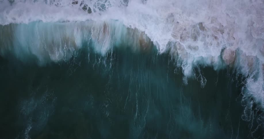 Waves slowly move tossing sand up as they crash