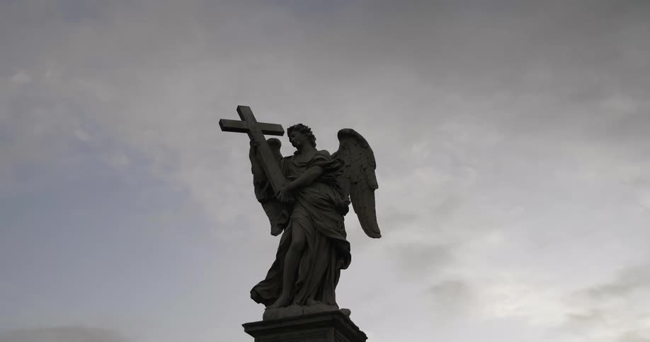 Clouds hover in the sky above a statue of an angel with a cross