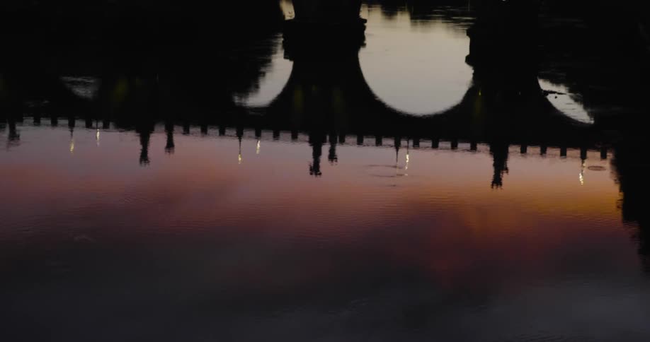 A bridge and sunset are being reflected in a river's surface